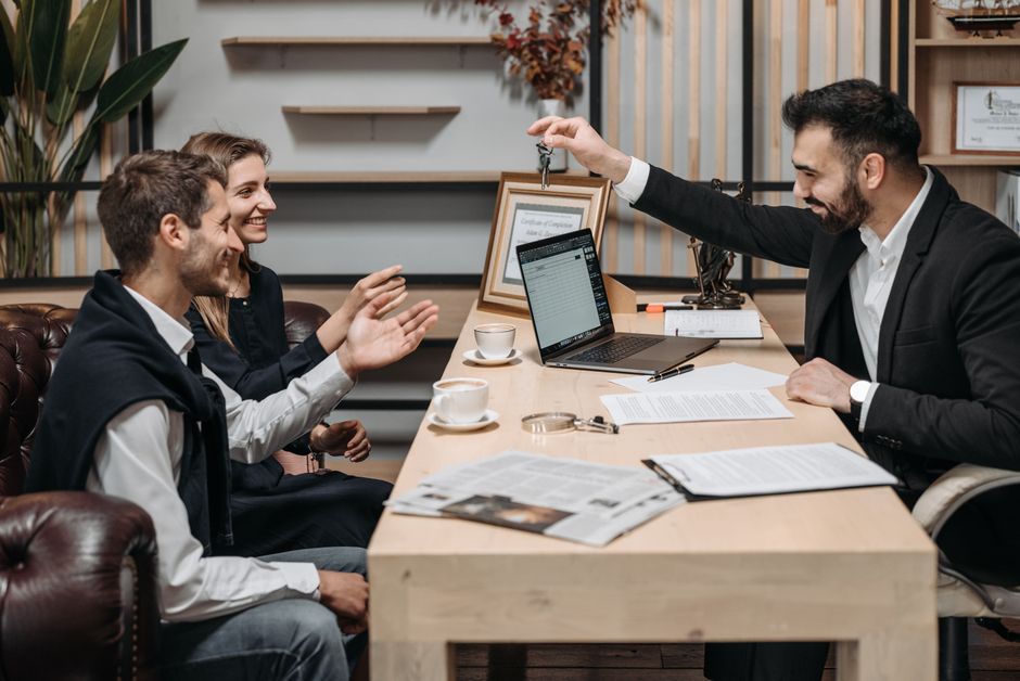 Smiling estate agent holding keys over a table with seated clients